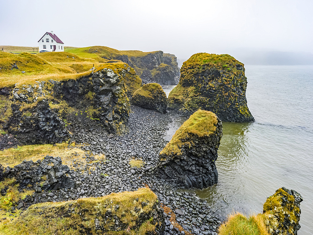 Rugged coastline of the Snaefellsnes Peninsula with a lone house along the cliffs in the mist; Snaefellsbaer, Western Region, Iceland