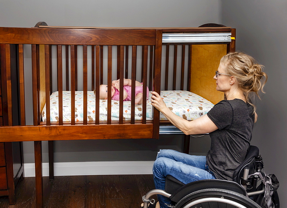 A paraplegic mom putting her baby down to sleep in a customized crib with a sliding door; Edmonton, Alberta, Canada