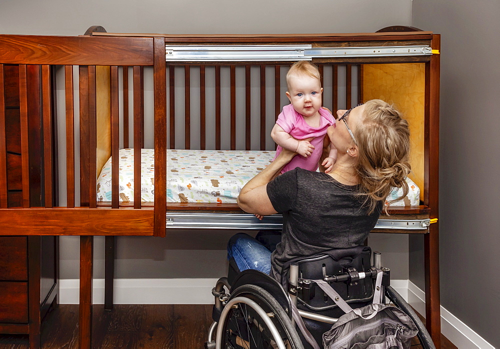 A paraplegic mother picking her baby up after a sleep in a customized crib with a sliding door; Edmonton, Alberta, Canada