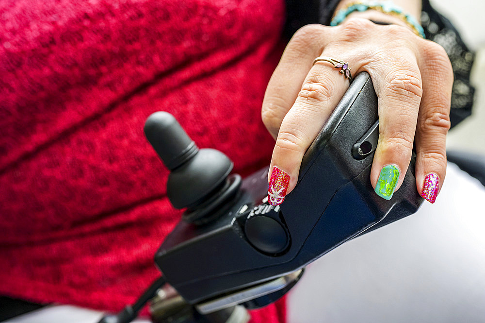 Maori woman with Cerebral Palsy in an electric wheelchair with a joystick and controllers, fingernails showing nail art; Wellington, New Zealand