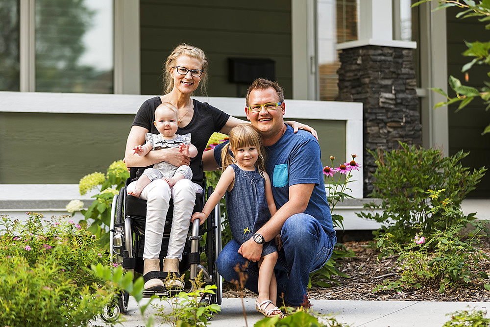 A young family posing for a family portrait outdoors in their front yard and the mother is a paraplegic in a wheelchair; Edmonton, Alberta, Canada