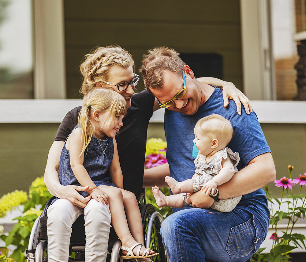 A young family posing for a family portrait outdoors in their front yard and the mother is a paraplegic in a wheelchair; Edmonton, Alberta, Canada