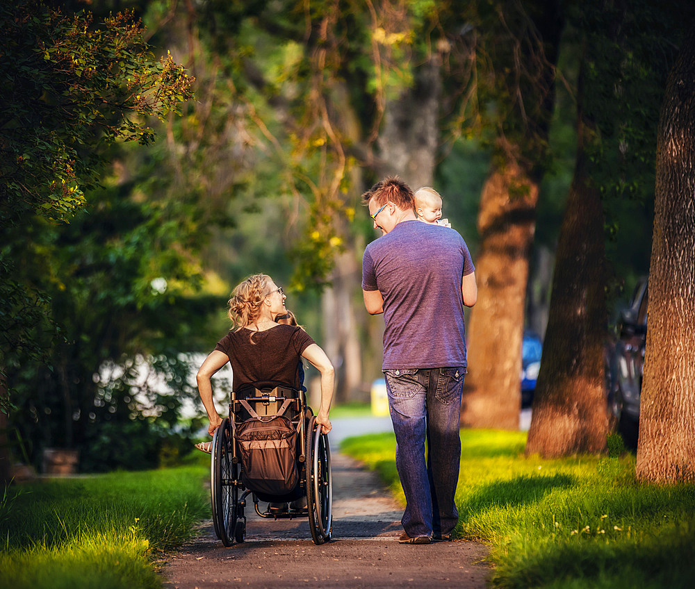 A view from behind of a family out walking in the evening and the mother is a paraplegic in a wheelchair; Edmonton, Alberta, Canada