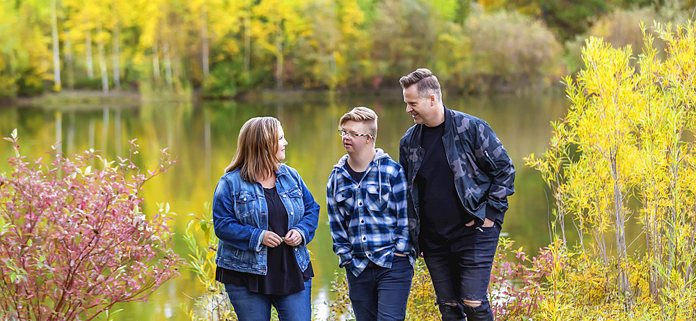 A young man with Down Syndrome walking with his father and mother while enjoying each other's company in a city park on a warm fall evening; Edmonton, Alberta, Canada