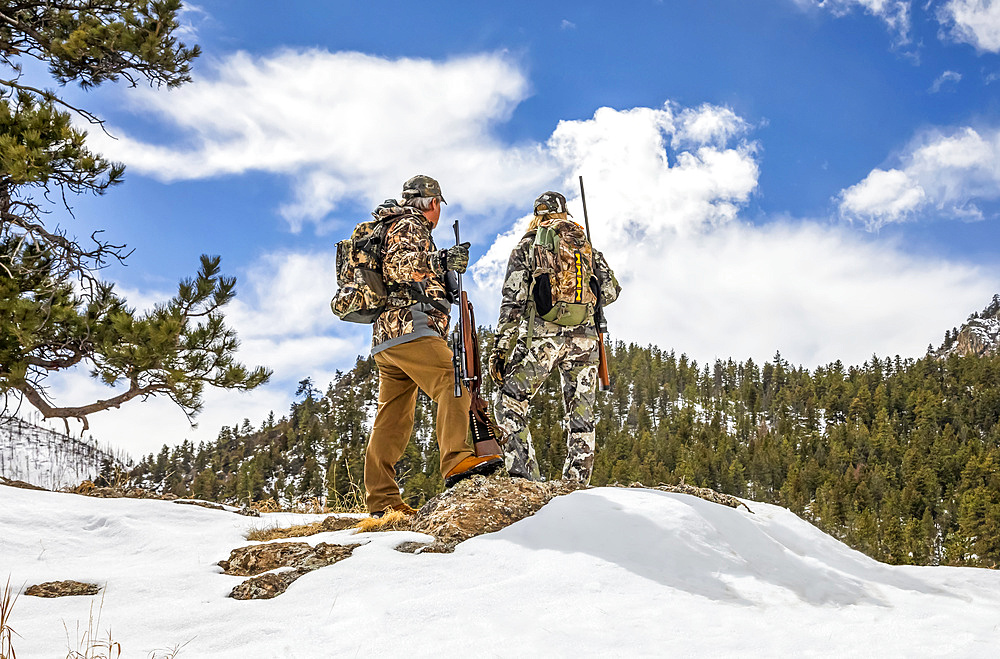 Hunters with camouflage clothing and rifle looking out to a forest; Denver, Colorado, United States of America