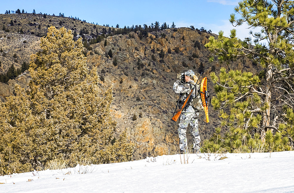 Hunter with camouflage clothing and rifle looking out with binoculars; Denver, Colorado, United States of America