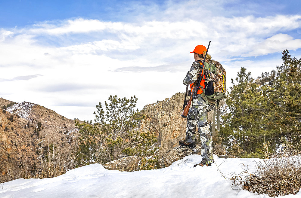 Hunter with camouflage clothing and rifle looking out in winter; Denver, Colorado, United States of America