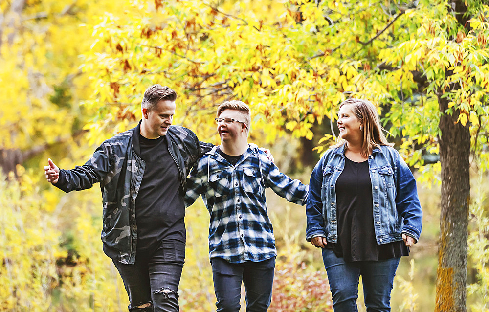 A young man with Down Syndrome walking with his father and mother while enjoying each other's company in a city park on a warm fall evening; Edmonton, Alberta, Canada