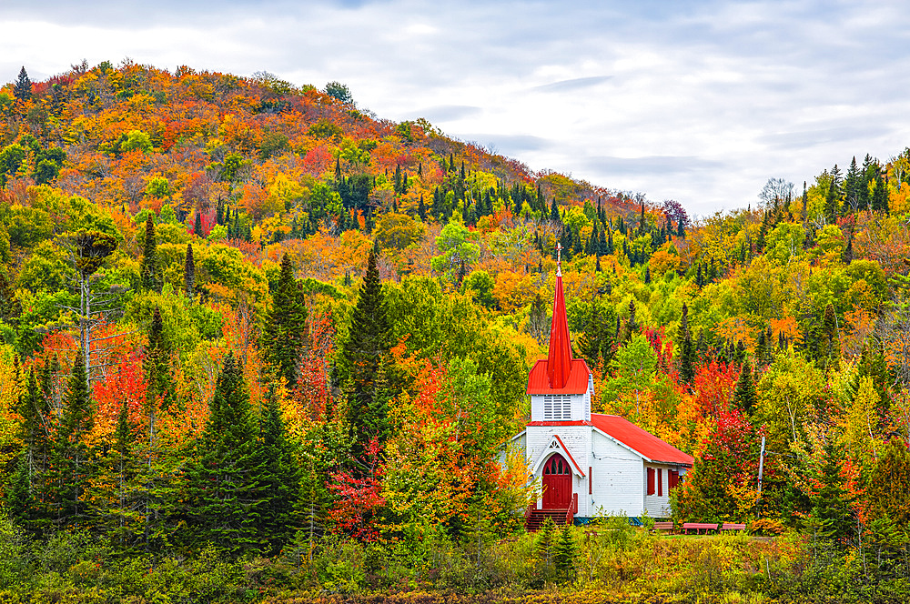 Country church in red and white hiding in the autumn coloured foliage in the hills; Sainte-Agathe-des-Monts, Quebec, Canada