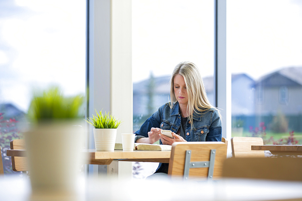 A mature Christian woman studying her bible in a coffee shop and doing some extra research on her smart phone: Edmonton, Alberta, Canada