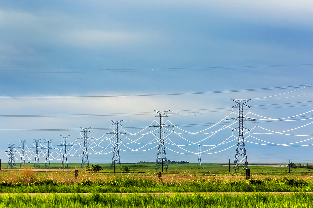 Highlighted power wires along large metal power towers with dark sky in the background, Yoho National Park; Field, British Columbia, Canada