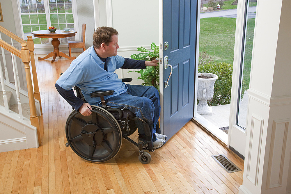 Man in a wheelchair opens the front door of his home and looks out