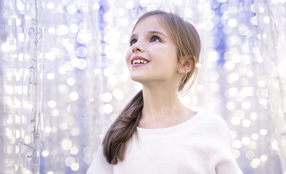 A young girl looks in wonder at white sparkling lights; Studio