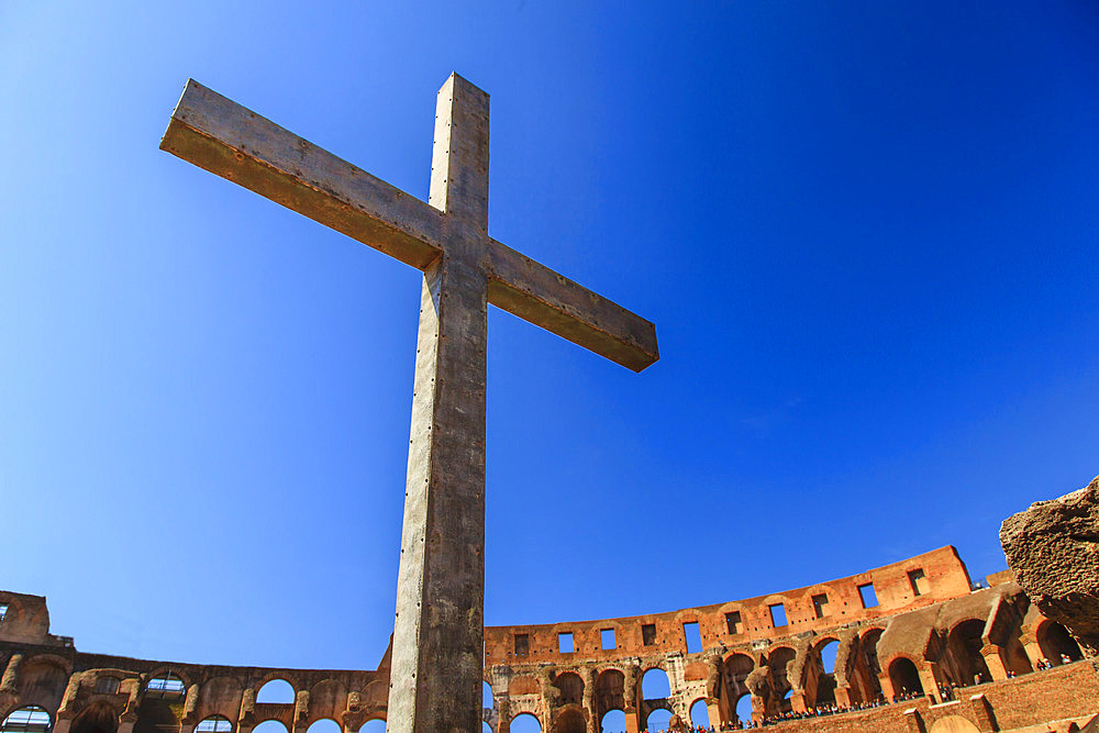 Close-up of a Christian cross inside the Roman Colosseum against a blue sky, erected by the Pope in 2000 to commemorate Christian Martyrs; Rome, Lazio, Italy