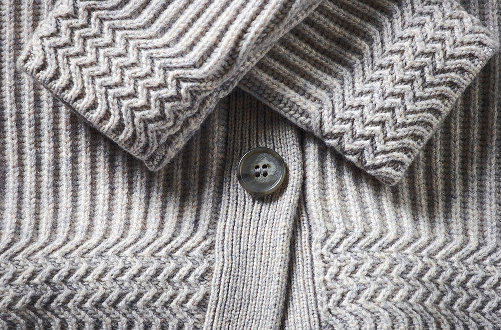 Extreme close-up of the cuffs and button on a grey knit sweater; Studio