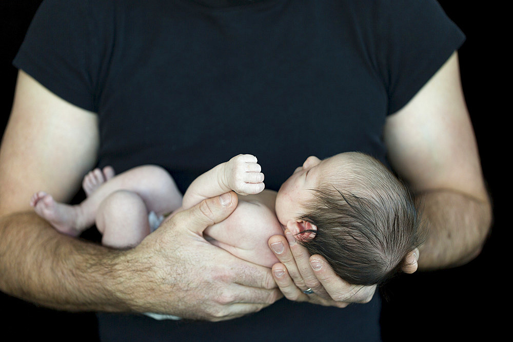 A father holding a newborn infant in his arms; Studio