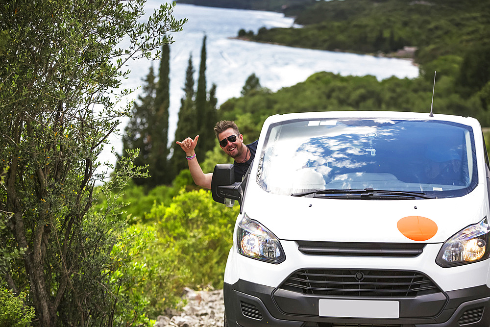 Man hanging out car window and driving camper van to find a secluded beach along the Croatia coastline; Zaton Doli, Dubrovnik-Neretva County (Dubrovacko-neretvanska zupanija), Croatia