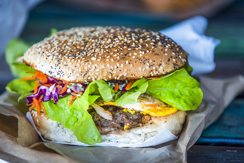 Close-up of a giant hamburger garnished with condiments and vegetables, Abel Tasman National Park; Tasman, New Zealand