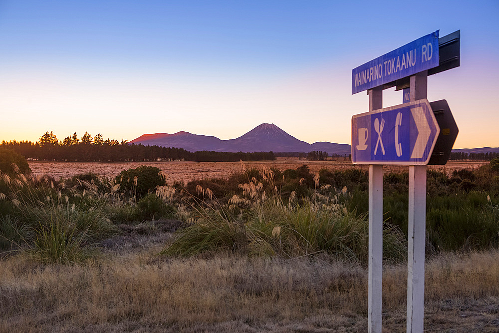 A beautiful sunset in the Tongariro National Park. The volcanic Mount Doom (Mount Ngauruhoe) can be seen in the background, with a roadside sign in the foreground; Manawatu-Wanganui, New Zealand