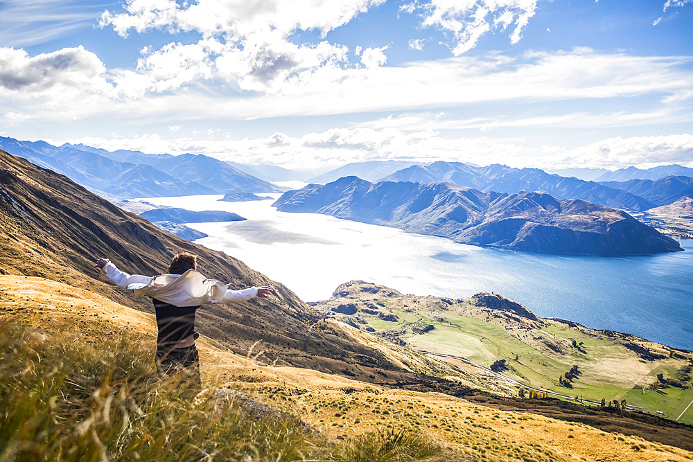 The strenuous yet highly rewarding hike to Roys Peak in Wanaka. The hike is difficult but the views are spectacular. A traveler celebrates at the summit; Wanaka, Otago, New Zealand