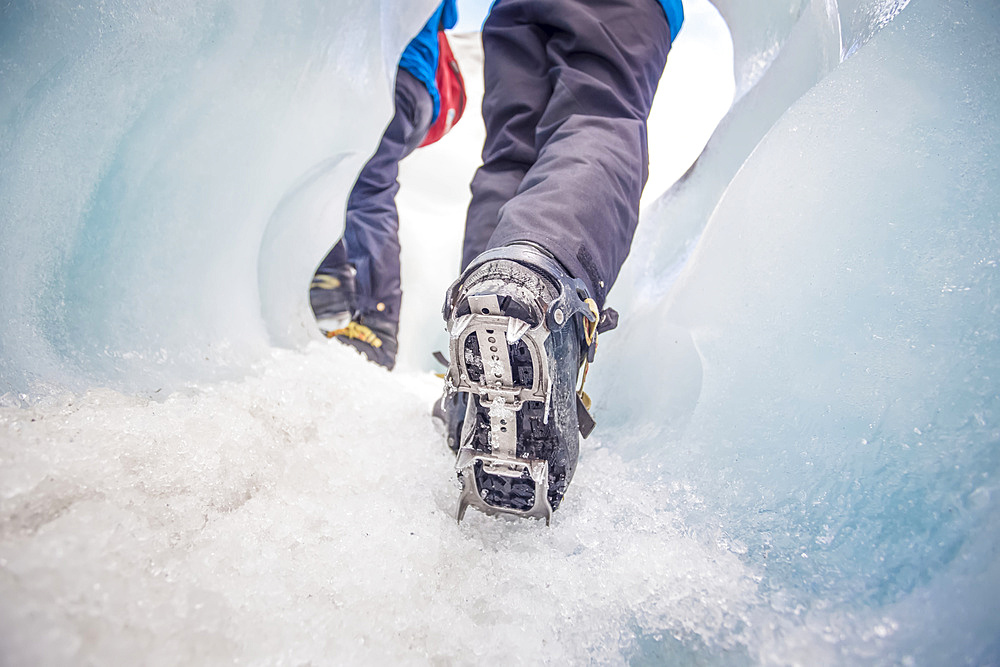 Close-up of person's feet wearing spiked traction cleats while walking on ice through the famous Franz Josef Glacier; West Coast, New Zealand