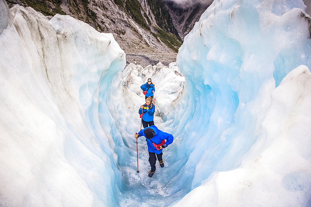 Travelers entering an ice tunnel while exploring the famous Franz Josef Glacier with its, blue ice caves, deep crevasses and tunnels that mark the ever changing ice formations; West Coast, New Zealand