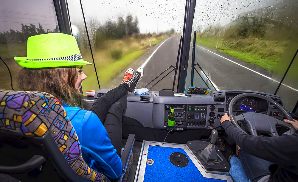 A girl sits in the front seat of a bus as they travel through New Zealand, Tongariro National Park; Manawatu-Wanganui, New Zealand