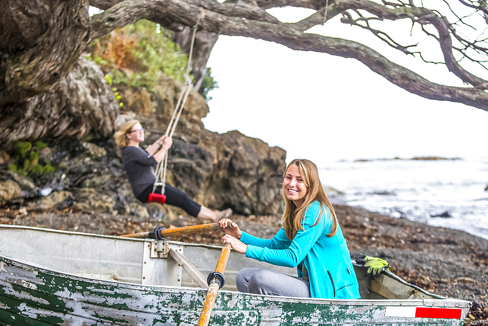 Girls sit and play in a beached boat on the eastern cape of New Zealand; Te Kaha, Bay Of Plenty, New Zealand