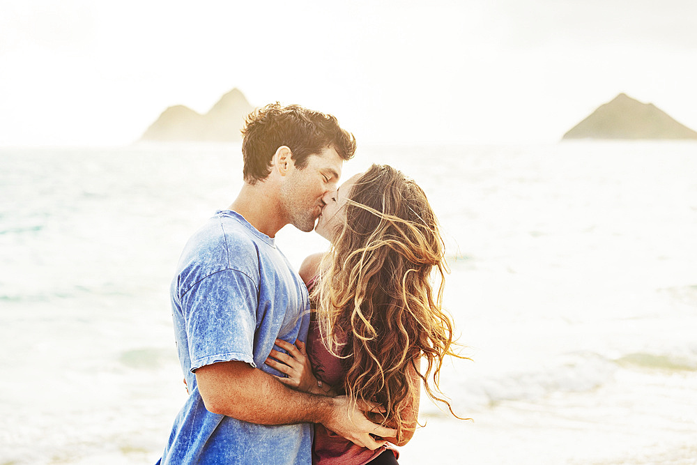 Millennial couple kissing on Lanikai Beach with the Mokes Islands in the background; Lanikai, Oahu, Hawaii, USA