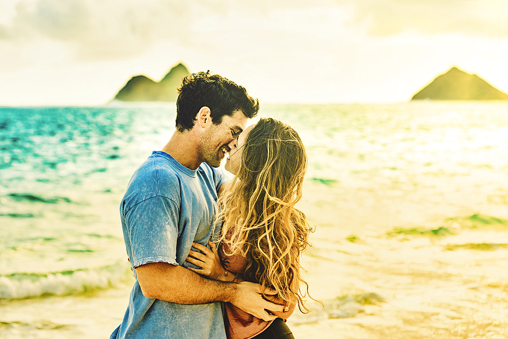 Millennial couple kissing on Lanikai Beach with the Mokes Islands in the background; Lanikai, Oahu, Hawaii, USA