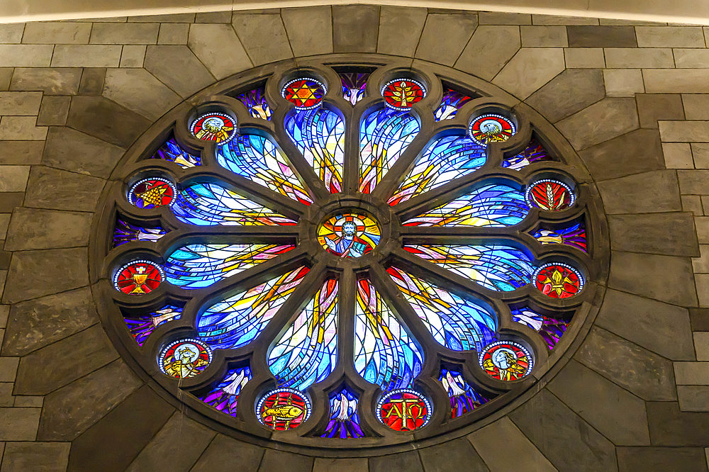 A colourful stained glass window in a circle-shape with intricate designs and symbols on a stone wall; Nelson, Nelson Province, New Zealand