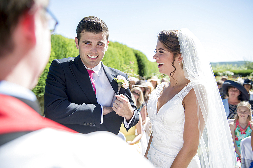 A bride and groom stand in front of a vicar at an outdoor wedding