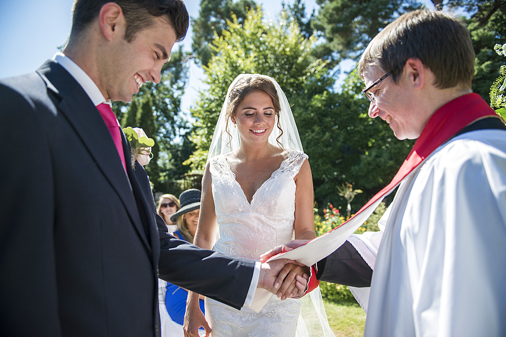 A bride and groom stand in front of a vicar at an outdoor wedding