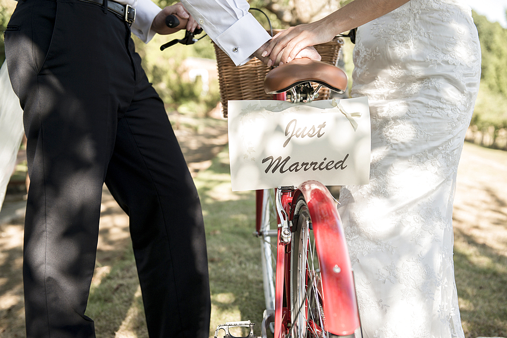 A bride and groom push a bicycle with a Just Married sign on the back