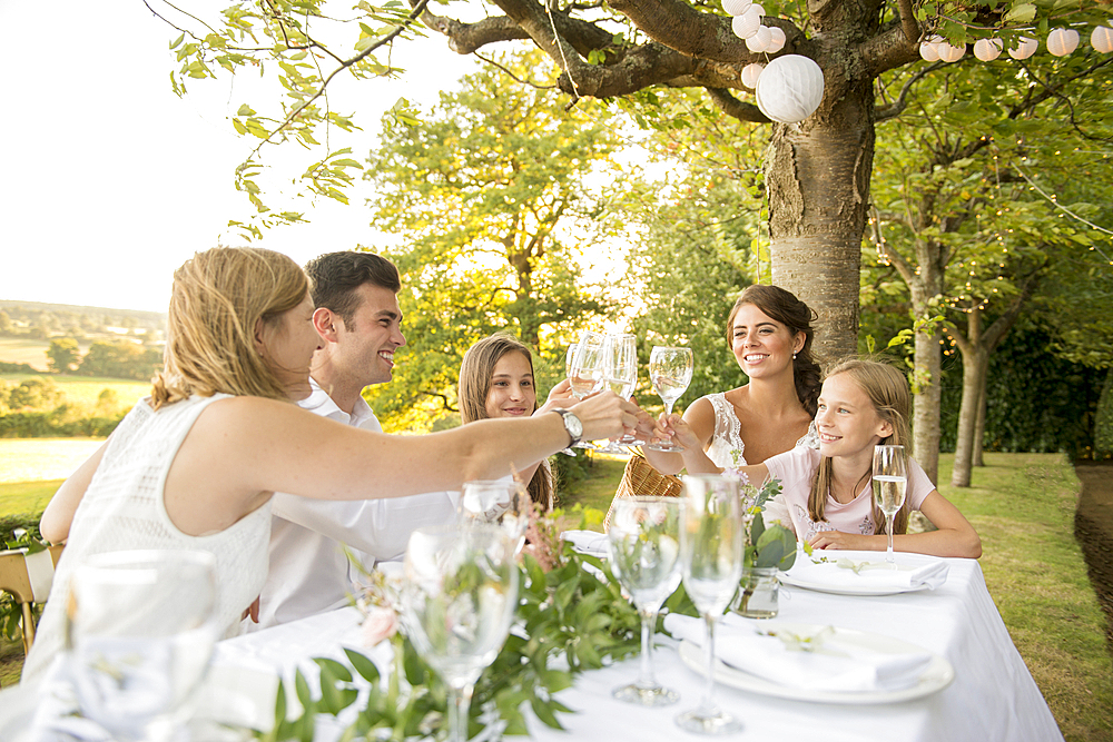 A bride and groom sitting at the top table with their friends at an outside wedding