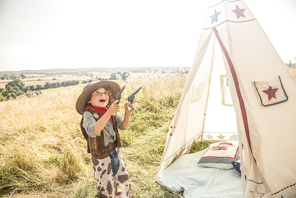 A young boy plays cowboys and indians outside in the sunshine