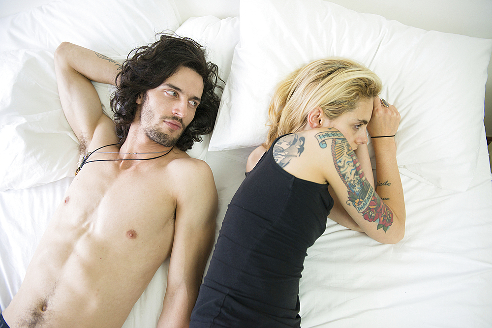 A young tattooed couple lying on a bed after an arguement.