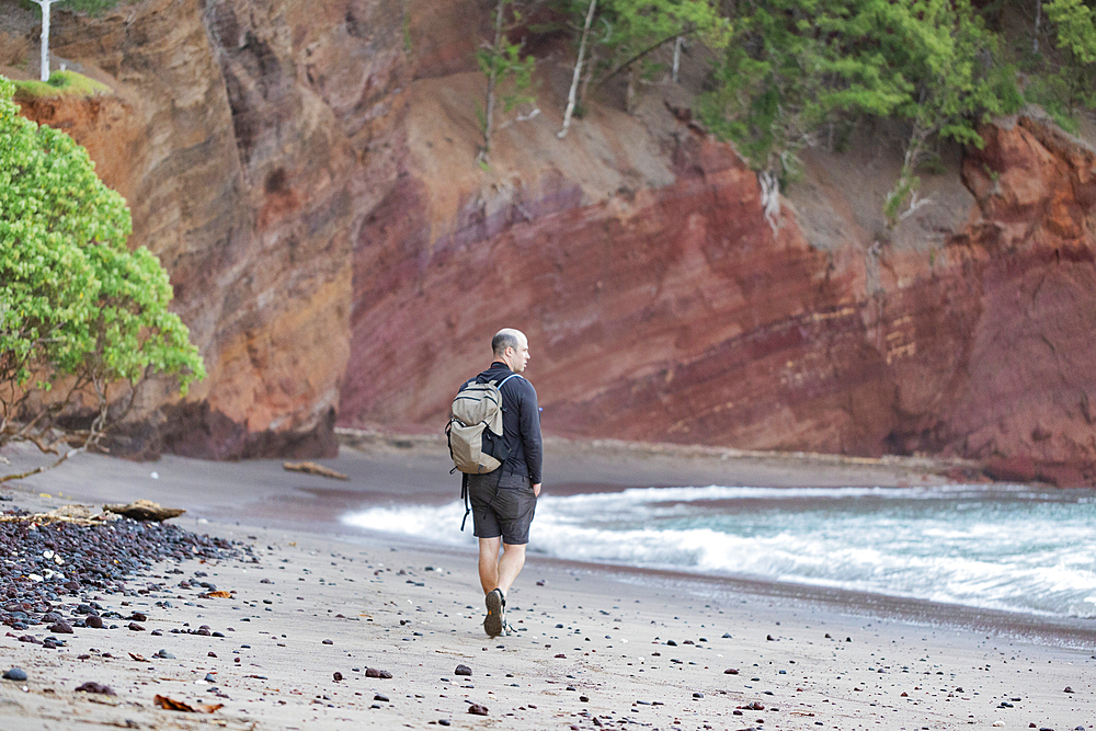 View from behind of a man walking along the beach among the rocky sea cliffs looking out at the Pacific Ocean on the Road to Hana, Maui, Hawaii, United States of America