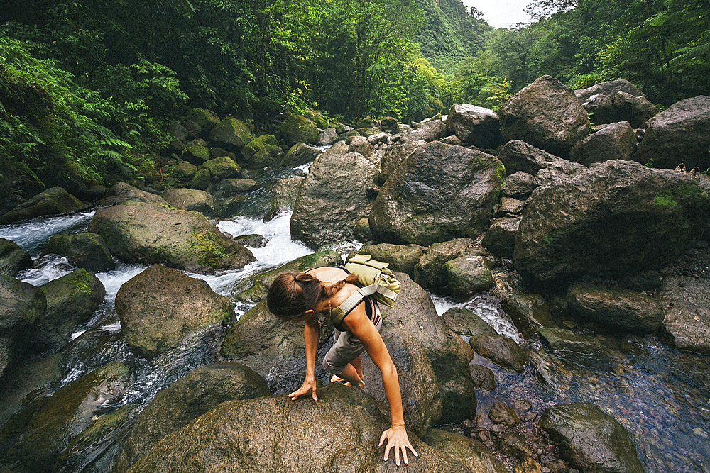 Overhead view of a woman climbing over the slippery, wet rocks along the rushing stream at Trafalgar Falls on the Caribbean Island of Dominica in Morne Trois Pitons National Park, Dominica, Caribbean