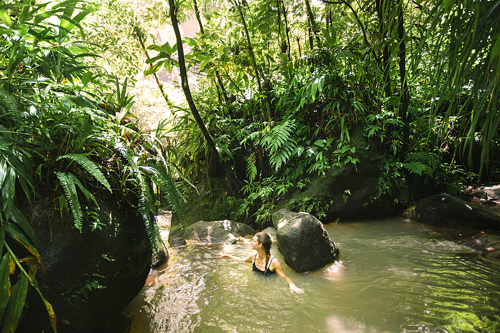 Woman enjoying soaking in the warm water, hot springs at Trafalgar Falls in the lush rainforest on the Caribbean Island of Dominica in Morne Trois Pitons National Park, Dominica, Caribbean