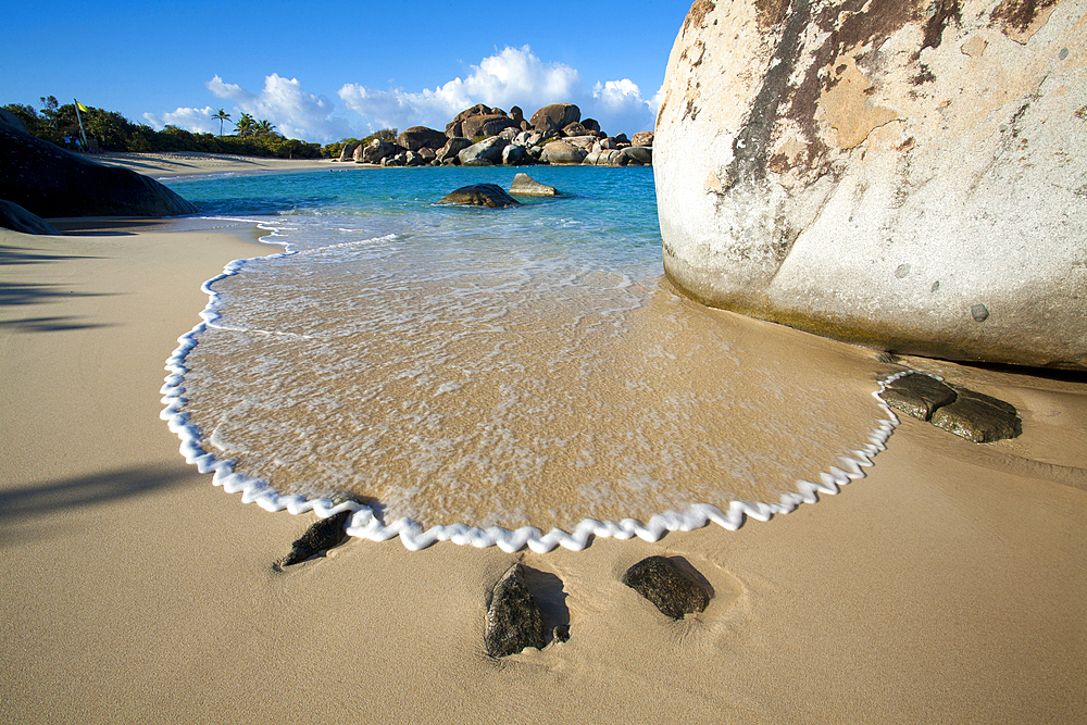 Stunning view of the sandy beach with surf forming a zigzag pattern in the foam next to the large, boulders lining the shores at The Baths, a famous beach in the BVI's, Virgin Gorda, British Virgin Islands, Caribbean