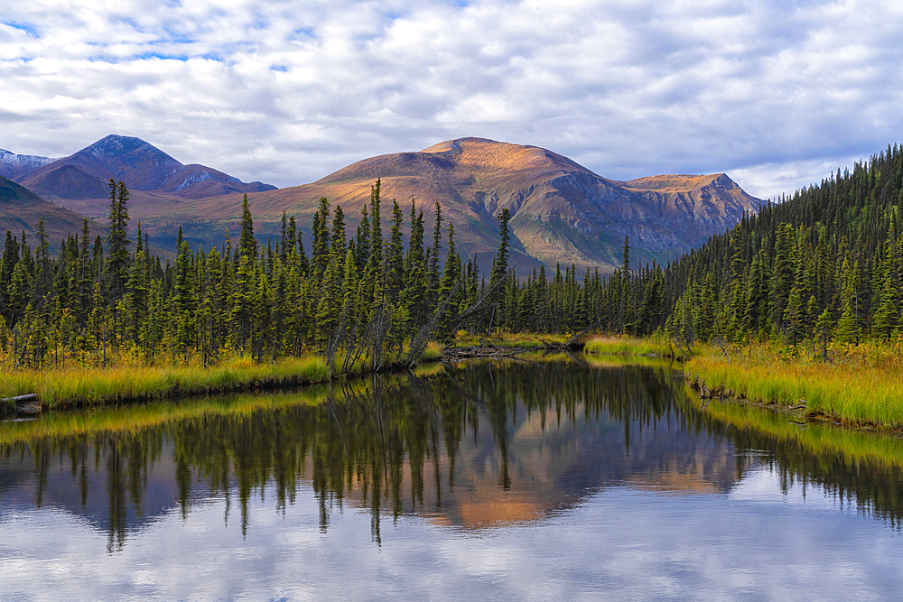 Scenic view of the serene wilderness at the end of a lake in the remote Yukon Territory with sunrise illuminating the mountain tops creating a beautiful reflection in the still waters, Yukon, Canada