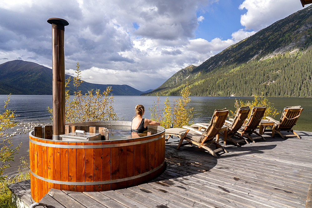 Woman sitting in a wood fired hot tub on the shore of a Yukon Lake, Yukon, Canada