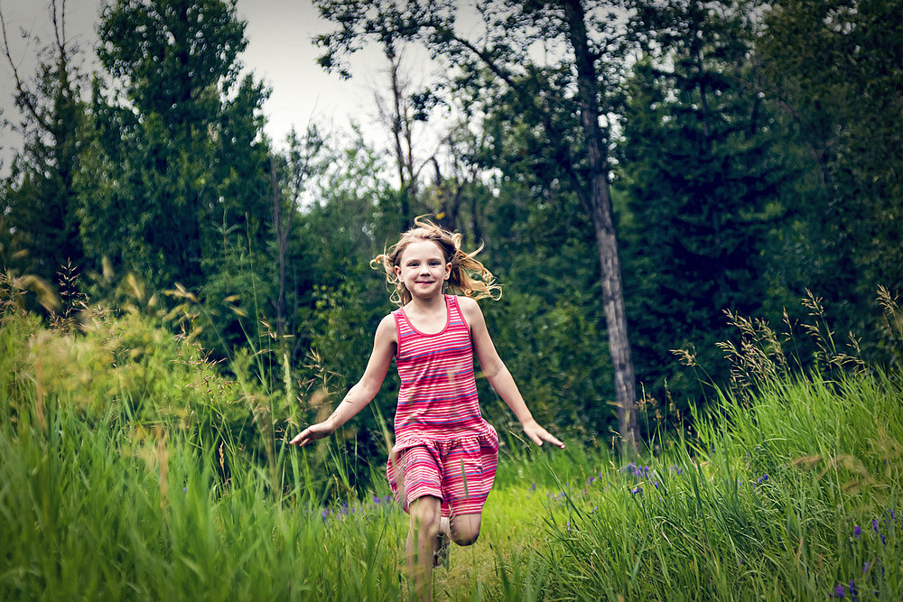 Portrait of a young girl running through the grass in a park, smiling at the camera, Edmonton, Alberta, Canada