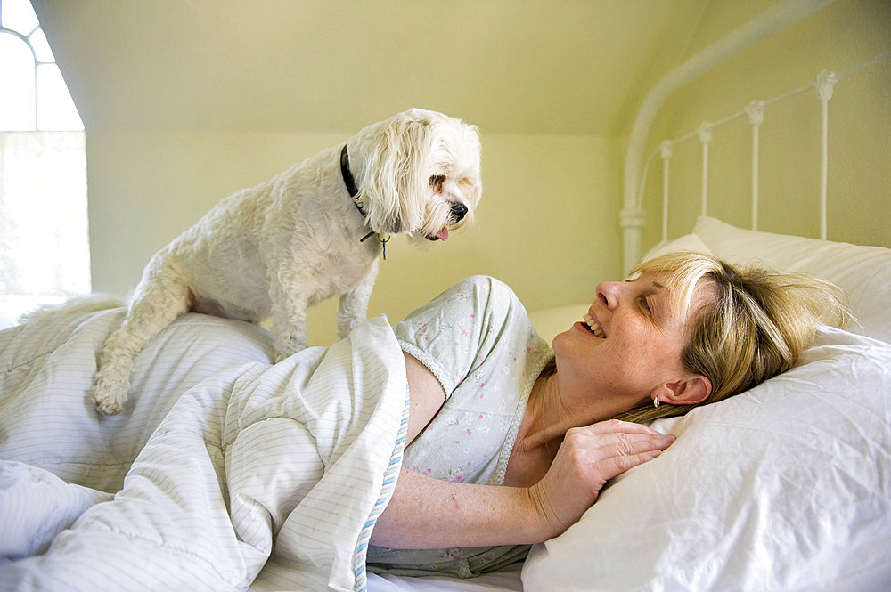 Woman lies in bed with her dog at their home, Lincoln, Nebraska, United States of America