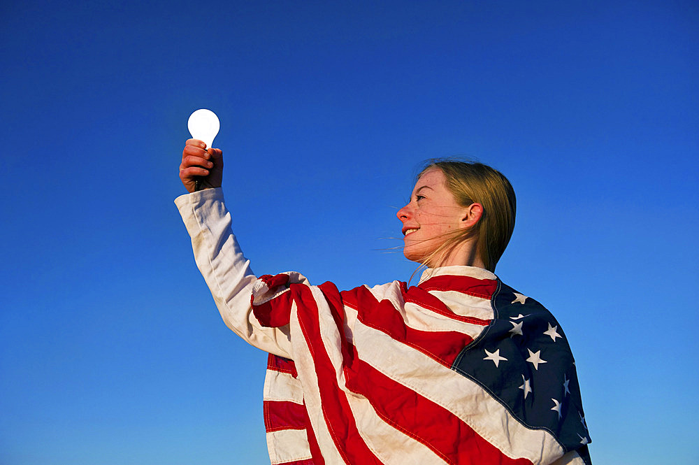 Light bulb shines in the hand of a girl wrapped in an American flag, Lincoln, Nebraska, United States of America