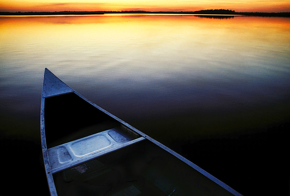 Canoe floats in placid waters along the bank of the St. Marys River as warm rays of sun fade after sunset. The river originates in the Okefenokee Swamp and flows toward the Atlantic Ocean forming a border between Florida and Georgia, United States of America