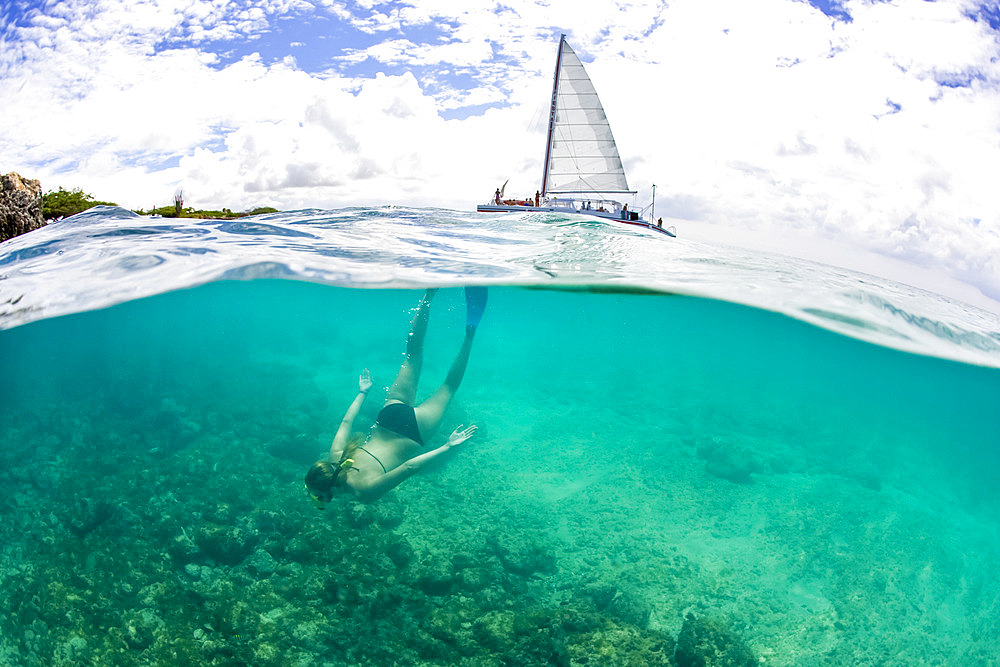 Split View of a teenage girl snorkeling in a bikini with a tour boat on the surface of the water above, Country of Aruba