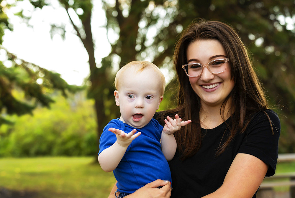 Outdoor portrait of an older sister spending quality time with her young brother who has Down Syndrome, in a city park during a warm fall afternoon, Leduc, Alberta, Canada