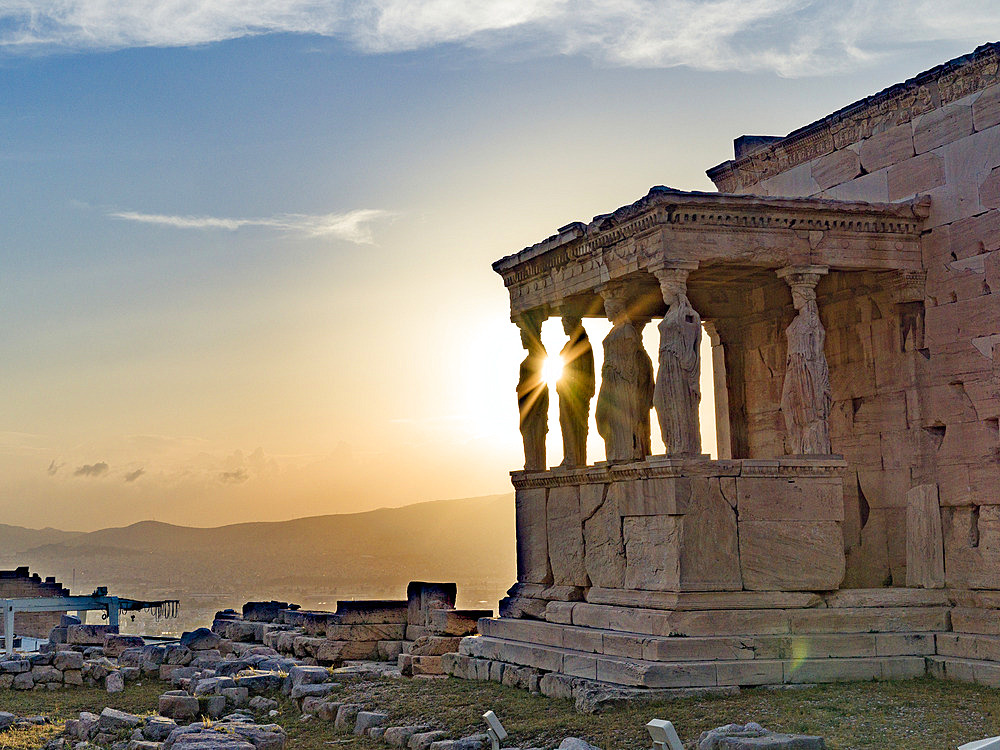 The Erechtheion (or Temple of Athena Polias) with sunburst on the Acropolis of Athens, the ancient citadel located on a rocky outcrop overlooking the City of Athens at twilight, Athens, Greece